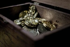 Guld- och silvermynt ligger i en öppen trälåda.